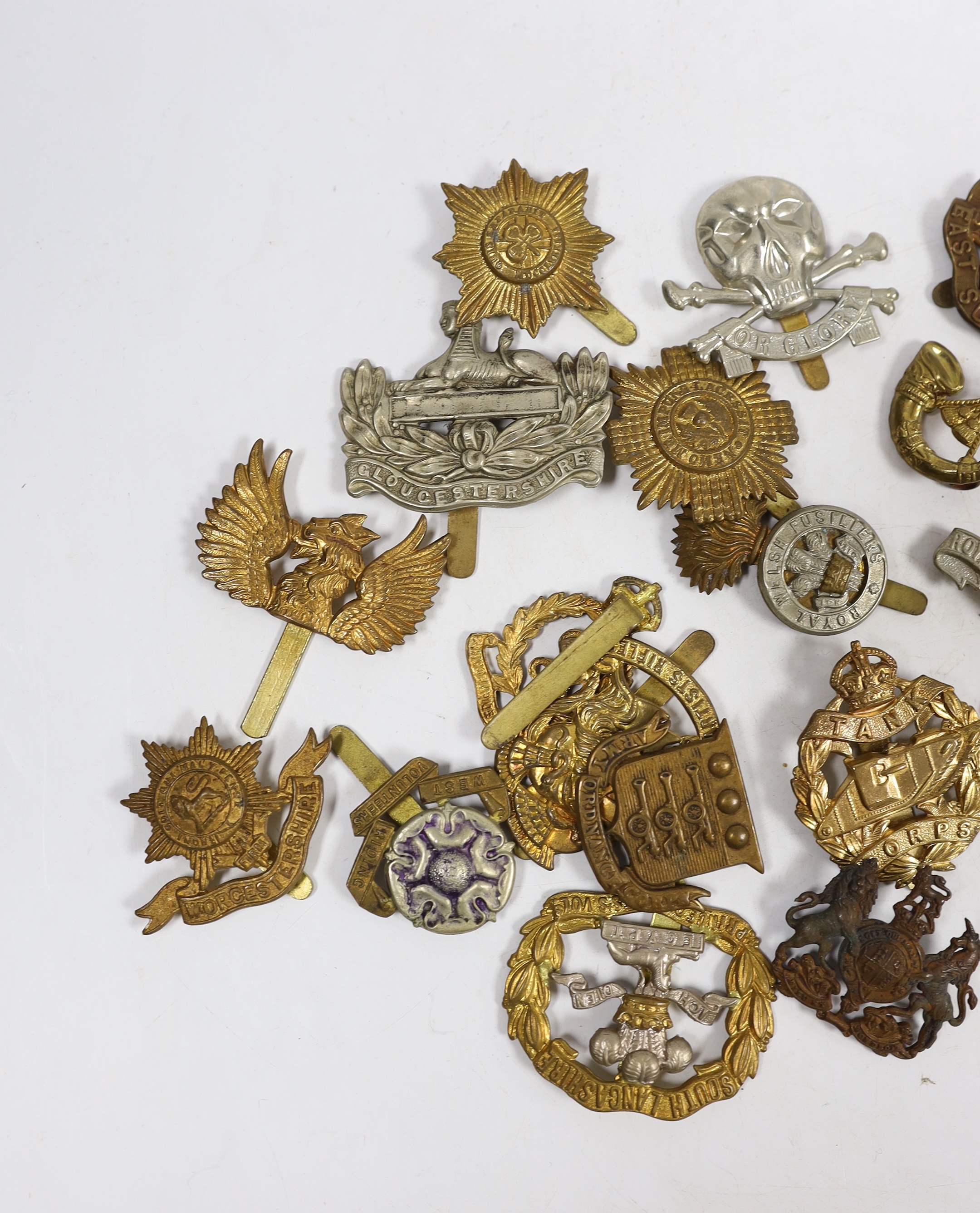 Twenty-five military cap badges including Gloucestershire Regiment, East Surrey, West Riding Volunteers, Wiltshire Regiment, Army Ordinance Corps, Worcestershire, Royal Warwickshire, Royal Dublin Fusiliers, RAMC, Royal W